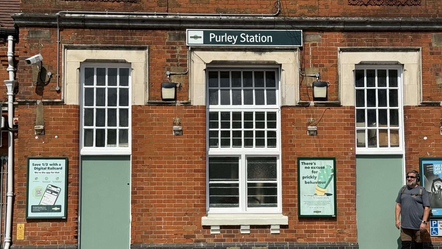 Purley Station entrance with red brick facade, station sign, and commuter standing outside on a sunny day